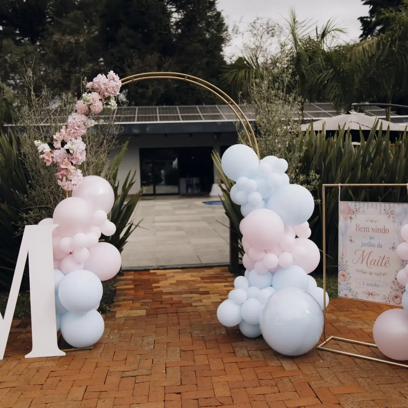 Entrada com arco de flores e balões no caminho de tijolos
