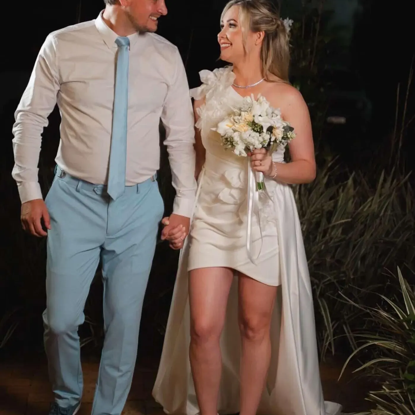 Casal de noivos de mãos dadas no jardim à noite