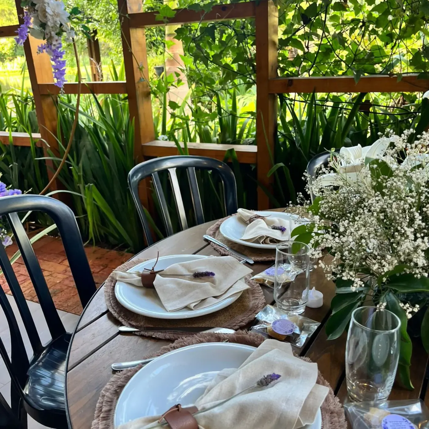Mesa posta com louças e flores, com a mata ao fundo